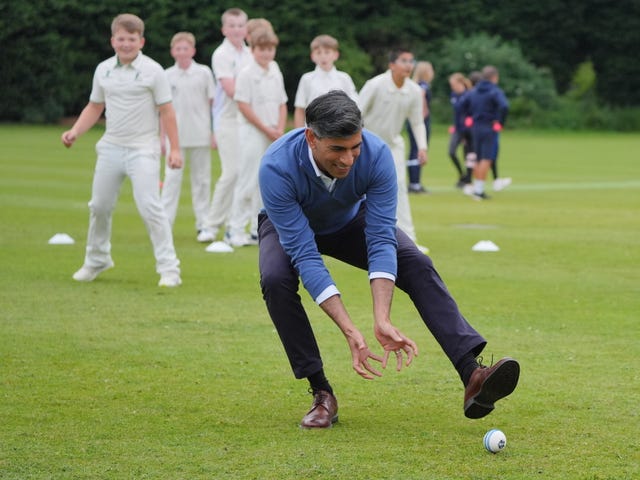 Rishi Sunak bends down to pick up a cricket ball while fielding during a training session