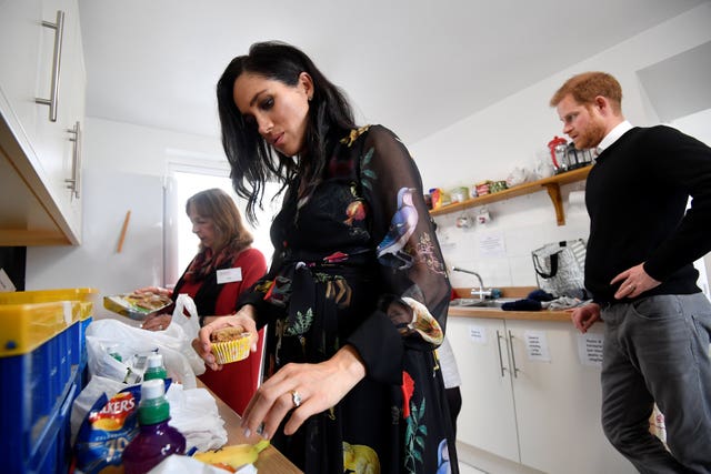 The Duchess of Sussex helps put together food parcels to go in the charity outreach van and prepares personalised messages on fruit in the charity kitchen during her visit to One25 