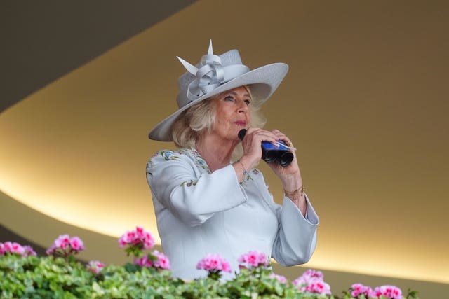 Camilla with binoculars, and wearing a fancy hat