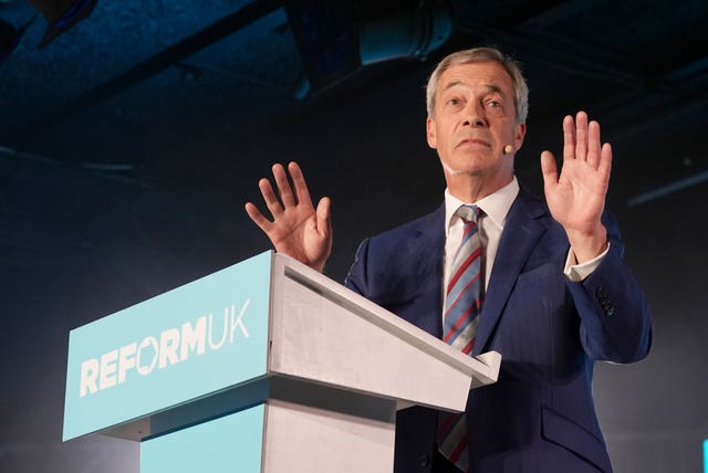 Nigel Farage with both palms raised, while speaking from a Reform UK lectern