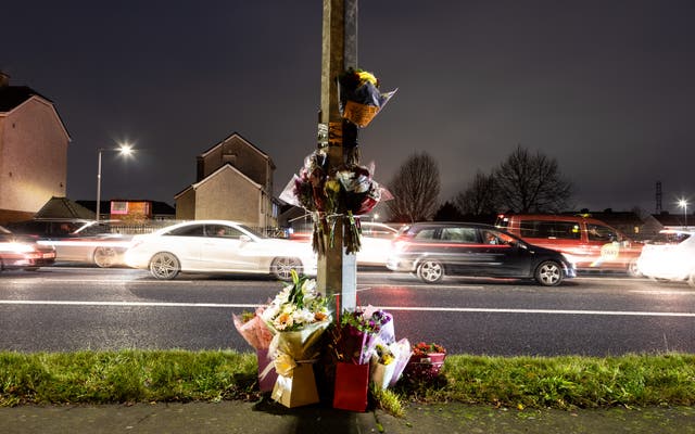 Floral tributes attached to a lamppost with cars in background