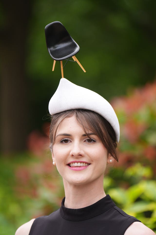 A woman wears a hat with a model of a chair perched on the edge