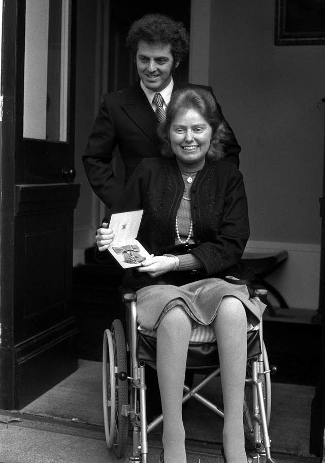 Black and white photo of Jacqueline du Pre in a wheelchair, with Daniel Barenboim behind her