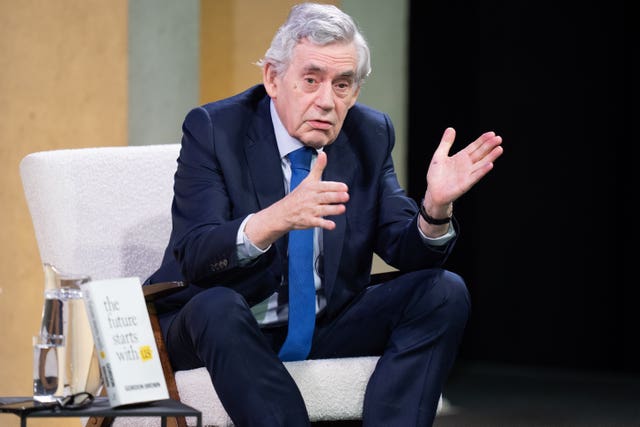 Gordon Brown gesturing with his hands while seated on a stage