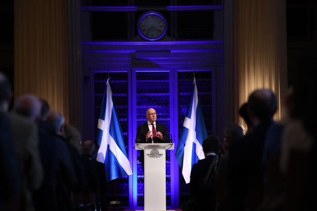 John Swinney gives a speech flanked by two saltire flags