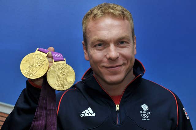 Sir Chris Hoy smiling as he holds up two gold medals from London 2023