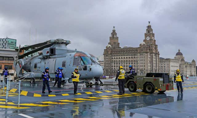 A Merlin helicopter is lifted on to the deck of the Royal Navy aircraft carrier HMS Prince of Wales as it sits in front of the Royal Liver Building in Liverpool