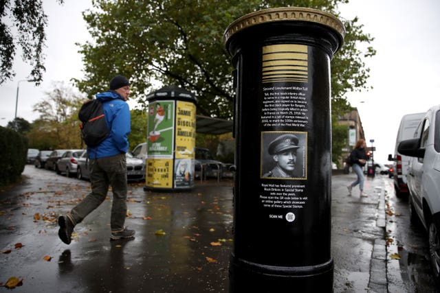 Members of the public walk past a black postbox featuring an image of Second Lieutenant Walter Tull, on Byres Road, Glasgow, one of four special edition postboxes unveiled by Royal Mail to mark Black History Month