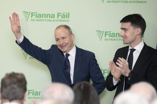 Micheal Martin smiling with one arm raised to wave, in front of Fianna Fail signage