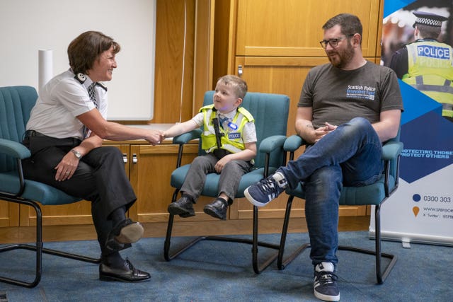 Boy, police officer and boy's father sitting in chairs with a police banner next to them