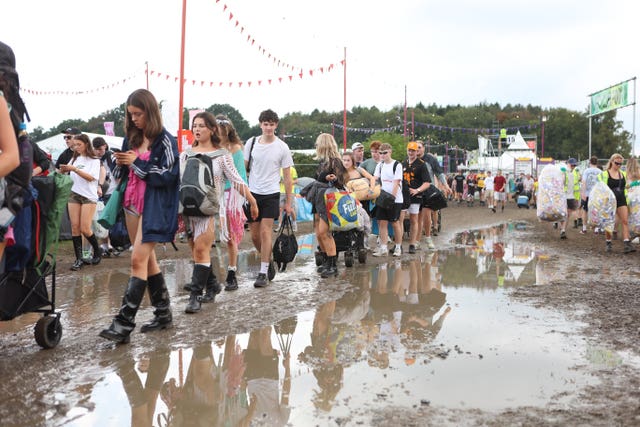 Festivalgoers walk round a large puddle in mud