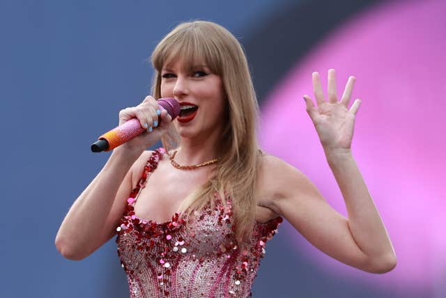 Taylor Swift wearing a pink performance outfit as she sings and waves to the crowd