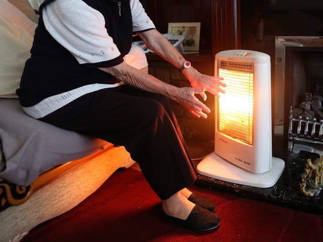 A woman warms her hands near an electric fire