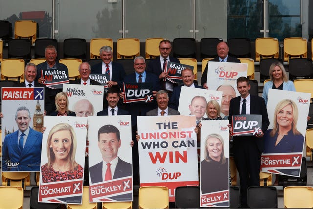 DUP election candidates holding campaign posters featuring their faces at the launch of the party's manifesto