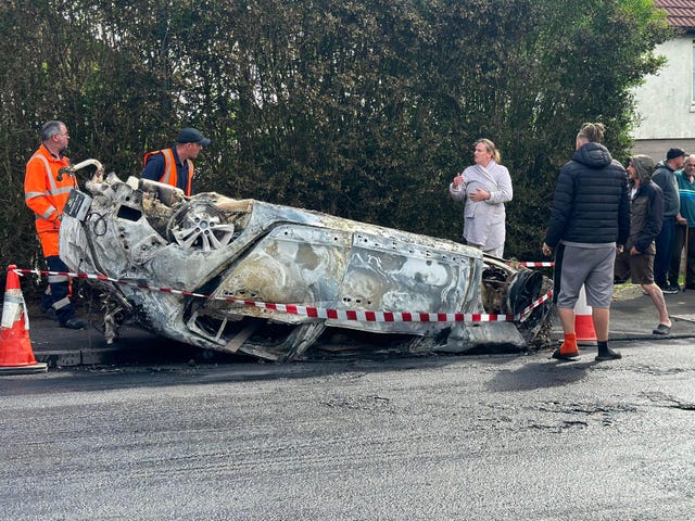 Council workers secure the area immediately around a car that was set alight following the deaths