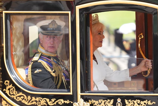 The King glances out of the window of the state coach as the Queen sits next to him