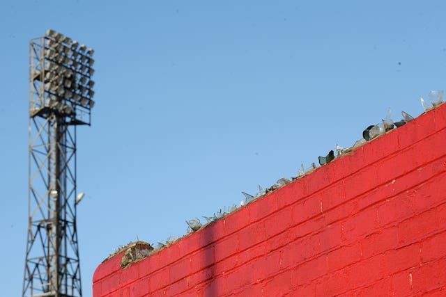 Detail of a floodlight and a wall topped with broken glass at a former Premier League ground
