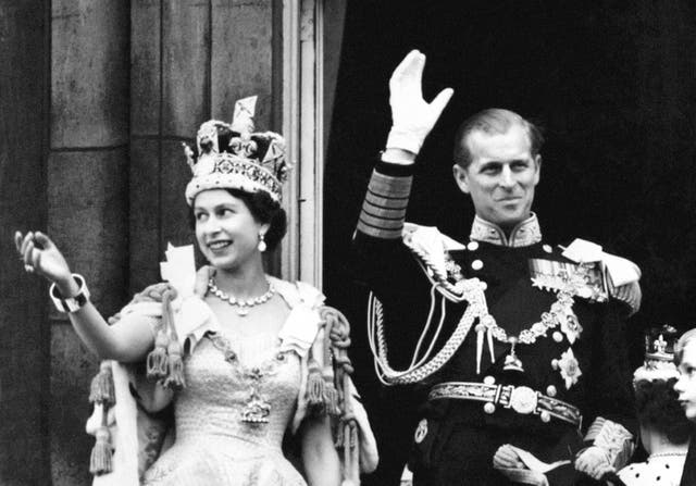 Queen Elizabeth II wearing the Imperial State Crown and the Duke of Edinburgh in uniform of Admiral of the Fleet wave from the balcony to the onlooking crowds around the gates of Buckingham Palace after the Coronation