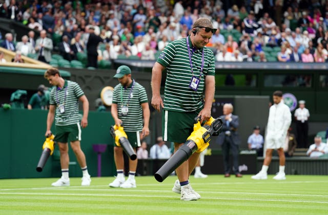 Ground staff use leaf blowers to attempt to dry the grass on Centre Court