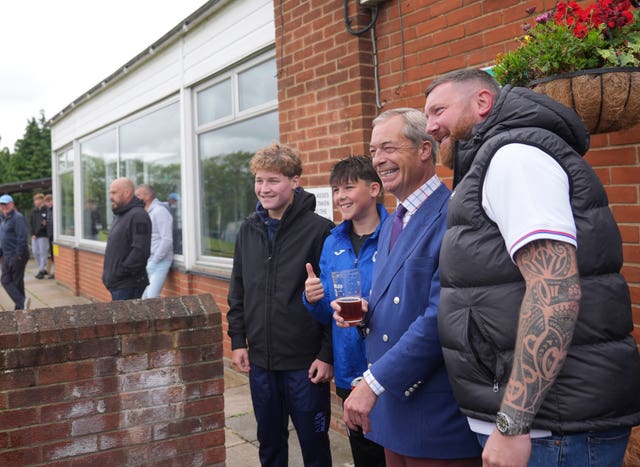 Nigel Farage with a pint in his hand posing for a photograph with a man and two boys