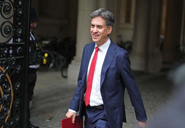 Ed Milliband in a blue suit and red tie carrying a red folder as he walks