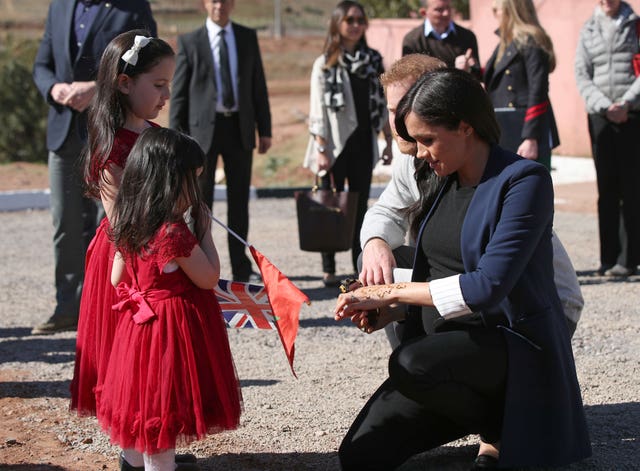 The Duchess of Sussex shows two girls her henna design