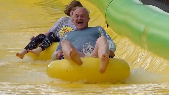 Sir Ed Davey smiles as he speeds down the Ultimate Slip n Slide attraction near Frome, Somerset in a rubber ring