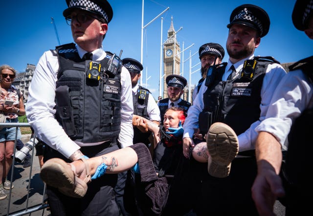 Five police officers carrying a protester away lifting her by her arms and legs