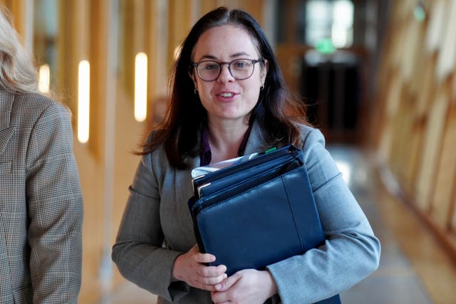 Kate Forbes smiling while walking through a corridor at Parliament, carrying folders