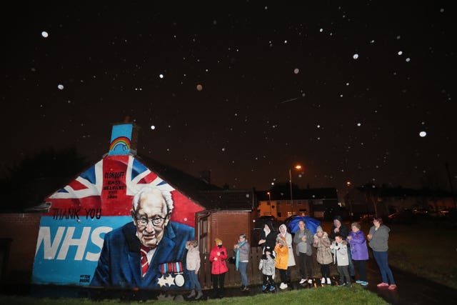 Local residents stand beside a mural of Captain Sir Tom Moore in Clonduff, east Belfast, as they join in with a nationwide clap