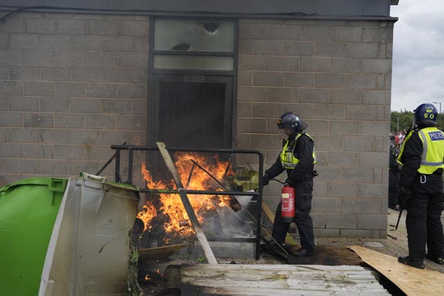 A fire is extinguished by police officers as trouble flares during an anti-immigration protest outside the Holiday Inn Express in Rotherham, South Yorkshire