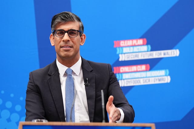 Rishi Sunak, wearing glasses, makes a speech in front of a blue background