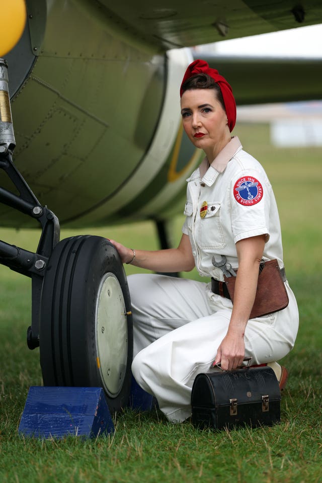 A woman in a Boeing Company outfit kneels at the wheel of a plane