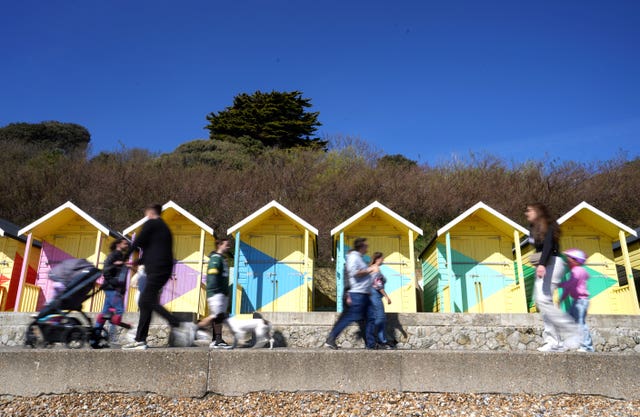 People walk past colourful beach huts, under a blue sky