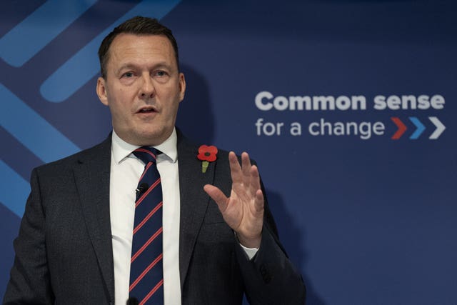 Russell Findlay gesturing with one hand while speaking in front of signage reading 'Common sense for a change'