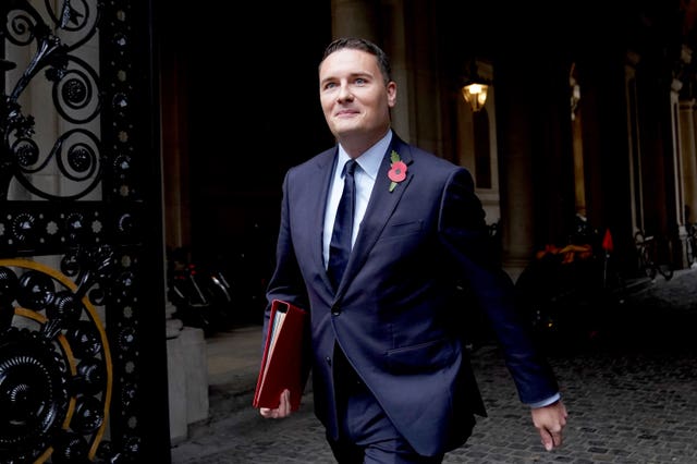 Wes Streeting walking while carrying a red Government folder under his arm