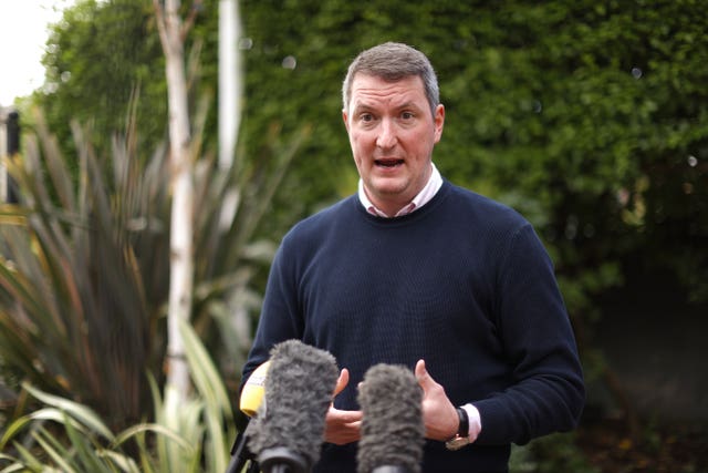 A man in a blue jumper speaks into two microphones