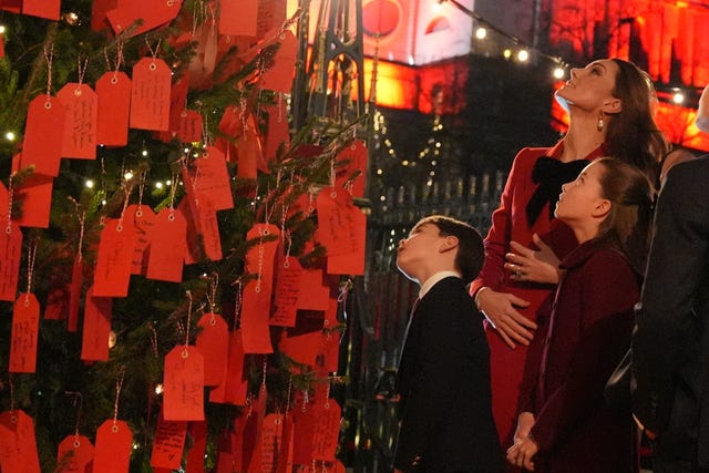 Kate, Charlotte and Louis looking up at a 'kindness tree' decorated in hundreds of labels, with containing messages to those who have shown kindness