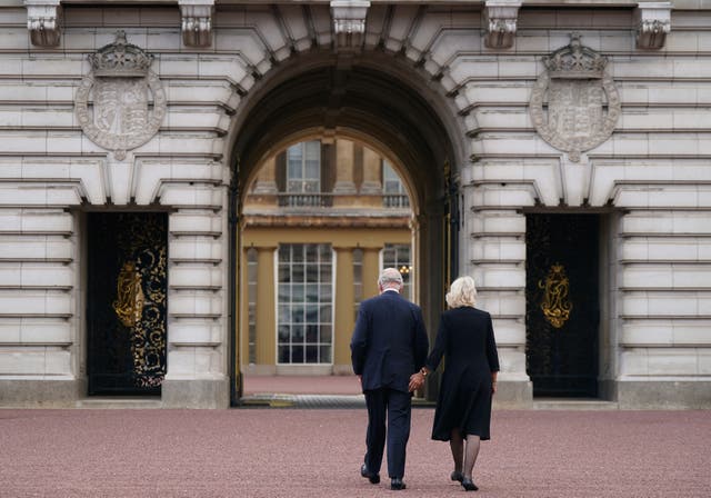 Charles and Camilla walk across the forecourt of Buckingham Palace 