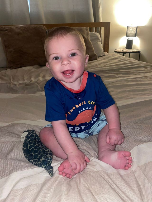 A smiling baby sitting on a bed