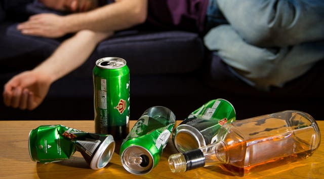 A man asleep on a sofa after while a number of empty lager cans sit on a table in front of him