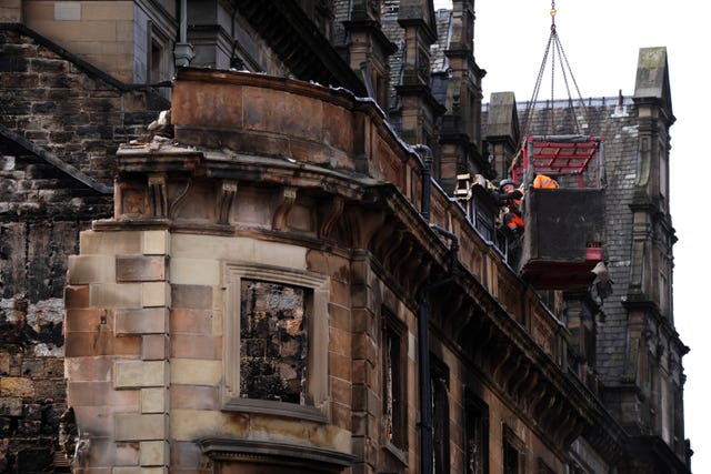 Workmen in the high basket remove stonework from a fire-damaged building