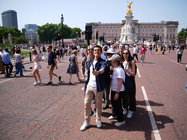 Tourists take a selfie in the sunshine in front of the Queen Victoria Memorial at Buckingham Palace in London