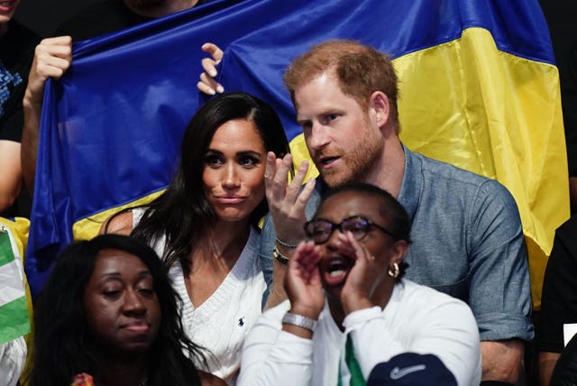 Harry and Meghan talk to one another as they sit in the stands watching the Invictus Games 