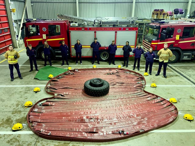 Cadets at Croxteth Community Fire Station beside a poppy made from hose, with a salvage sheet used to create the leaf, remembering the war dead on Armistice Day