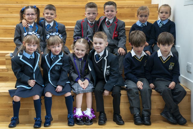 Six sets of twins, all dressed in school uniform, sit on steps