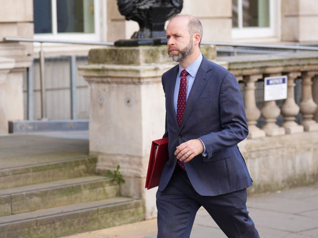 Business and Trade Secretary Jonathan Reynolds wearing a suit and walking with a red Government folder under his right arm