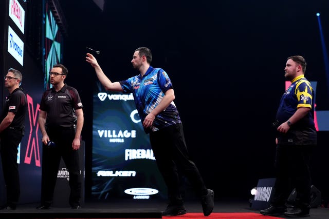 Luke Humphries throws a dart as Luke Littler and the scorers look on