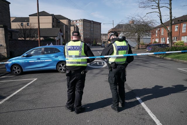 Two police officers standing beside police tape on a road