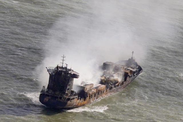 View of a burnt-out container ship smoking, while adrift at sea